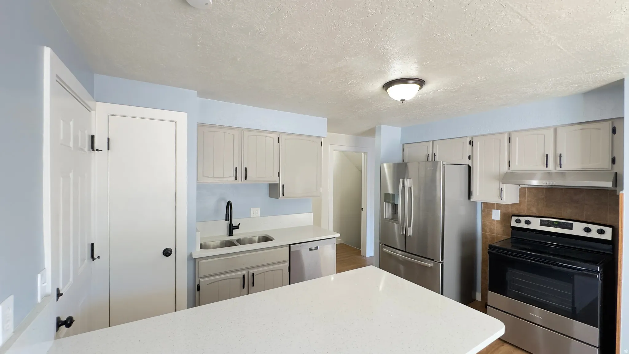 Kitchen featuring white cabinetry, stainless steel appliances, a white countertop island, and a dual-basin sink with a matte black faucet