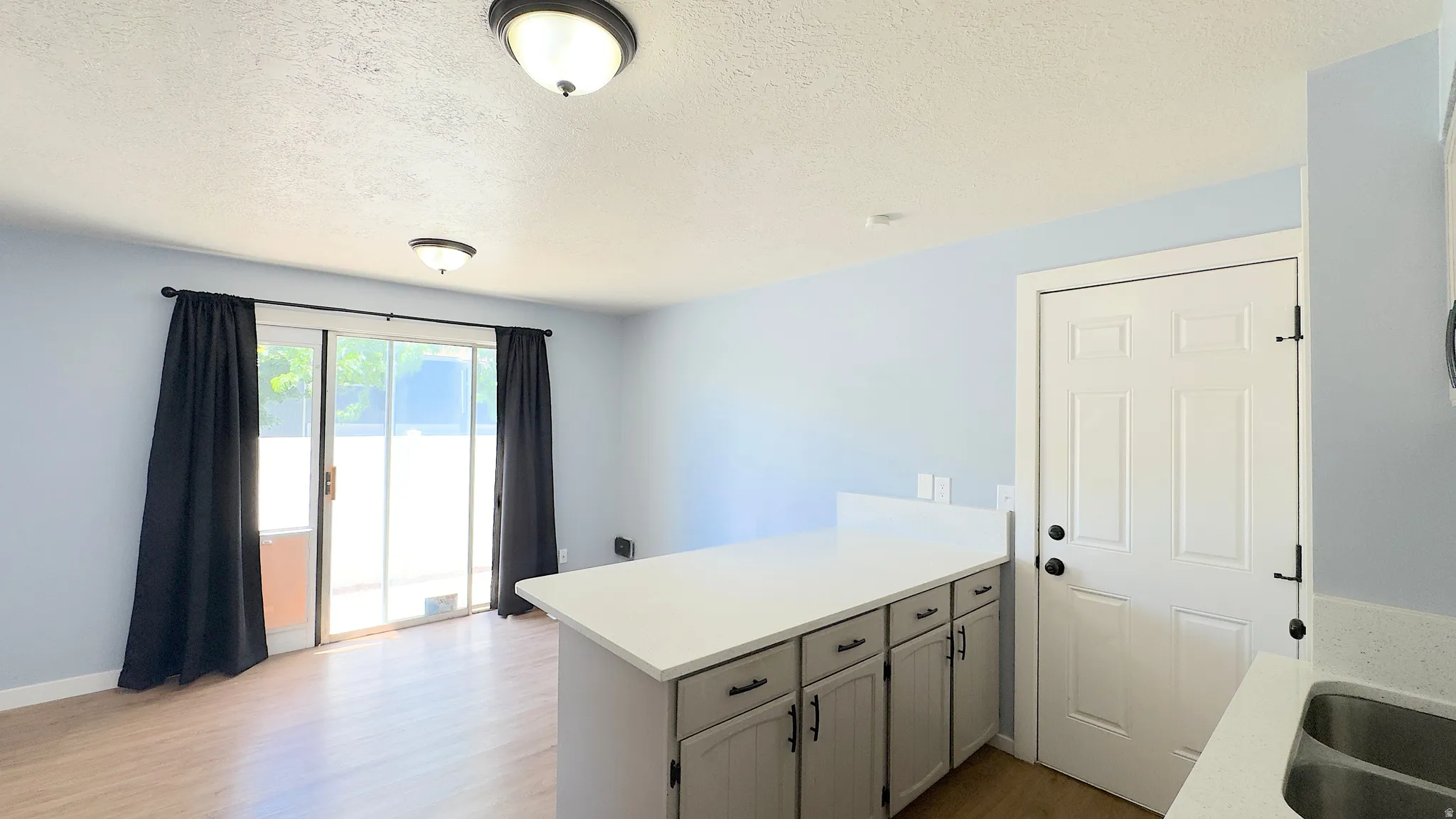 Dining Room Area just off kitchen. Open-concept living space featuring wood-finish flooring, white kitchen island with countertop, and sliding glass door access to private patio.