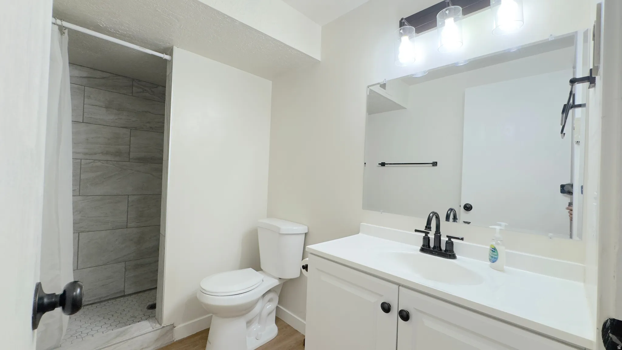 Hall way 3/4 bathroom featuring a white vanity with a single basin, a large wall-mounted mirror, and a three-light fixture with exposed bulbs.