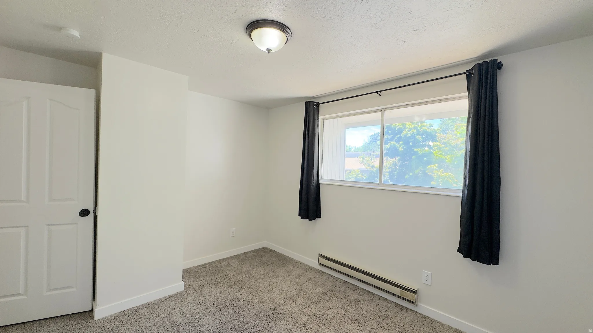 Bright interior space featuring a double window with exterior tree-lined scenery, neutral carpeting, white baseboards, and a paneled white door.