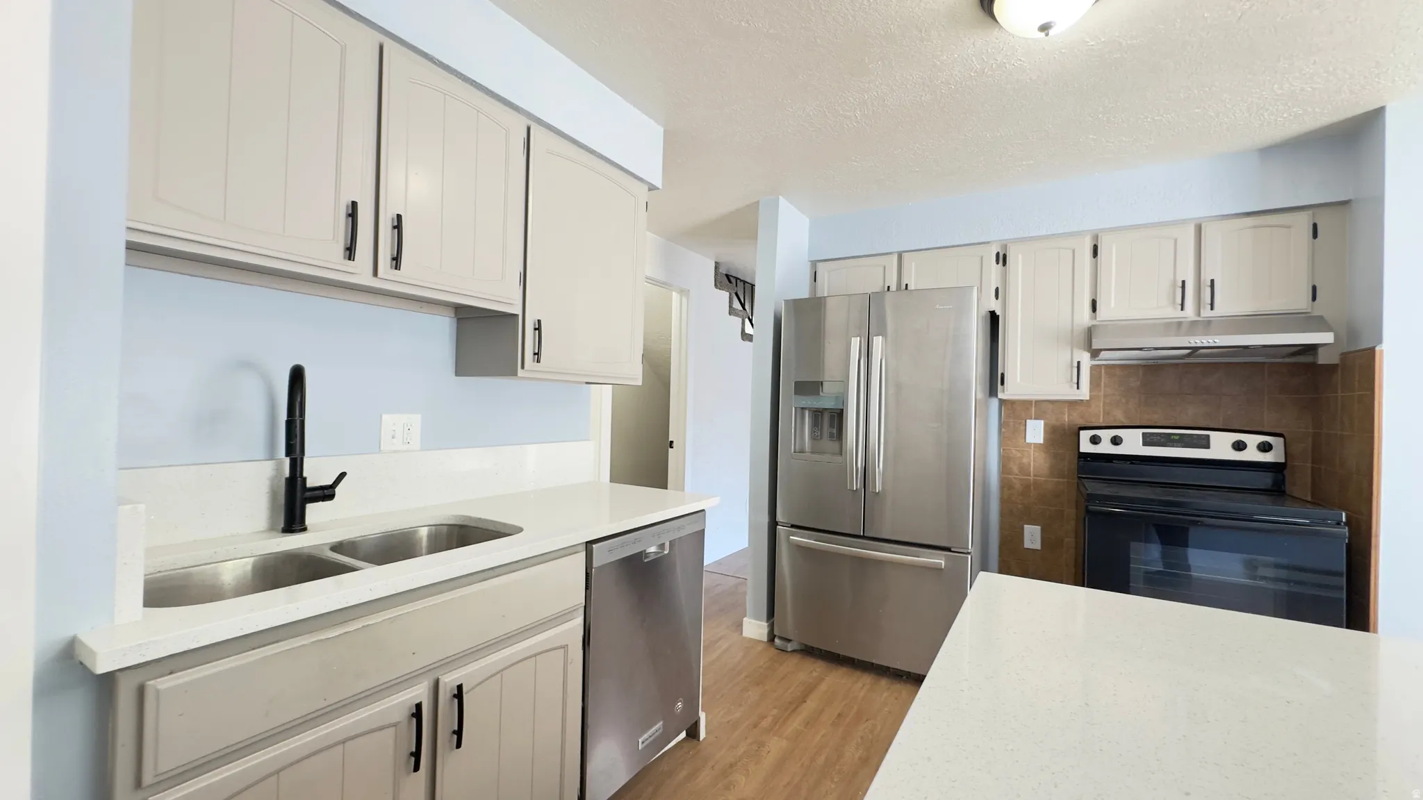 Kitchen featuring light gray cabinetry, stainless steel appliances, white corian countertops, and wood-finish flooring.