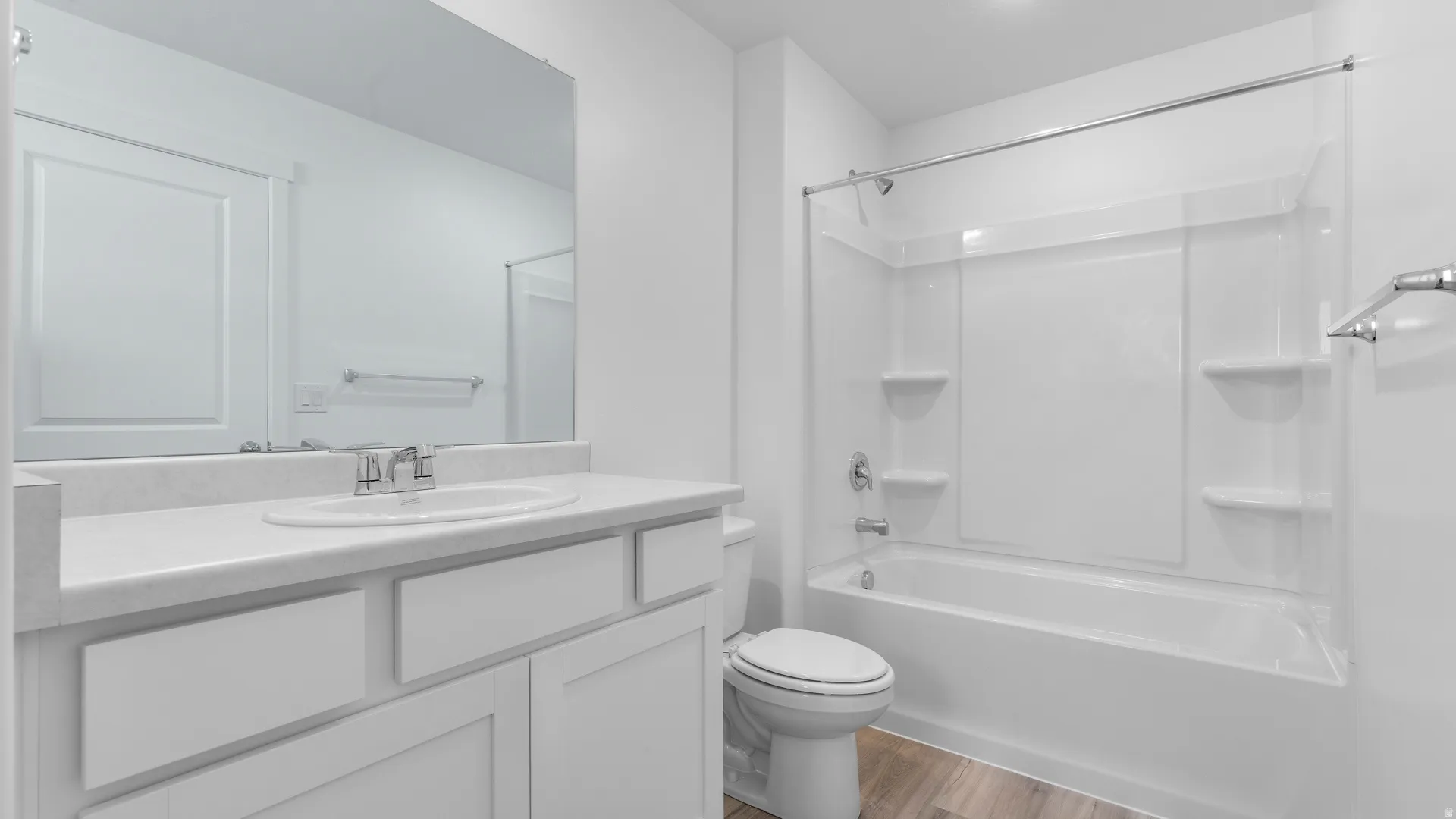 Full bathroom featuring a single vanity with an undermount sink, a large mirror, a toilet, and a combined bathtub and shower unit with a wall-mounted showerhead and faucet