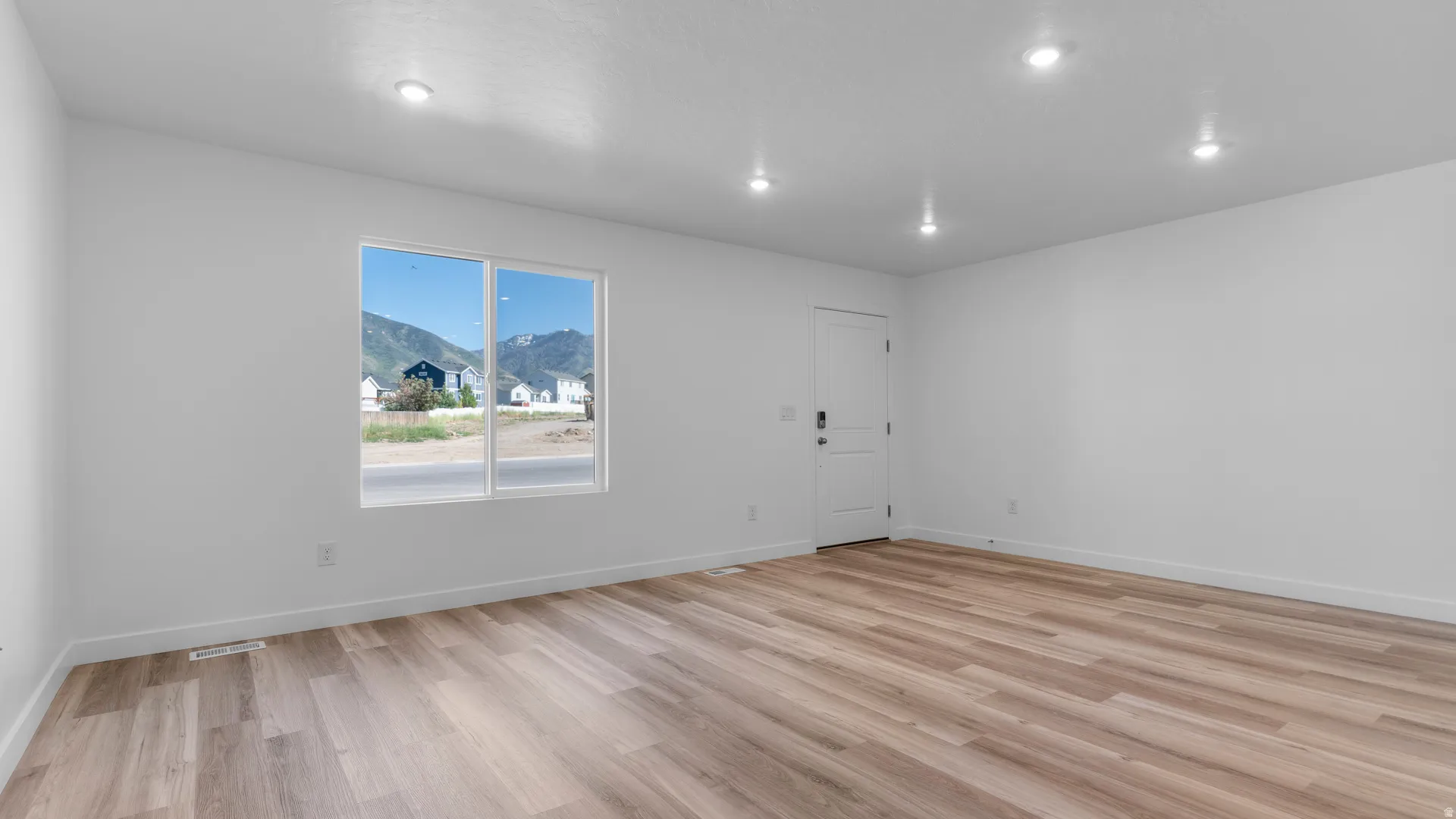 Spacious room featuring wood-finish flooring, recessed ceiling lighting, a white painted door, and a multi-pane window with a mountain backdrop