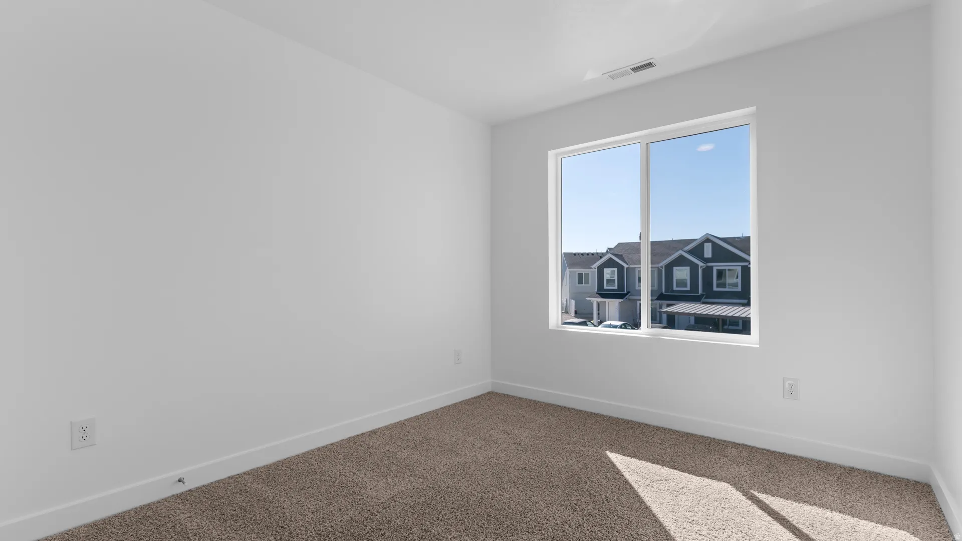 Bright room featuring a large horizontal window, white walls, and light brown carpeting