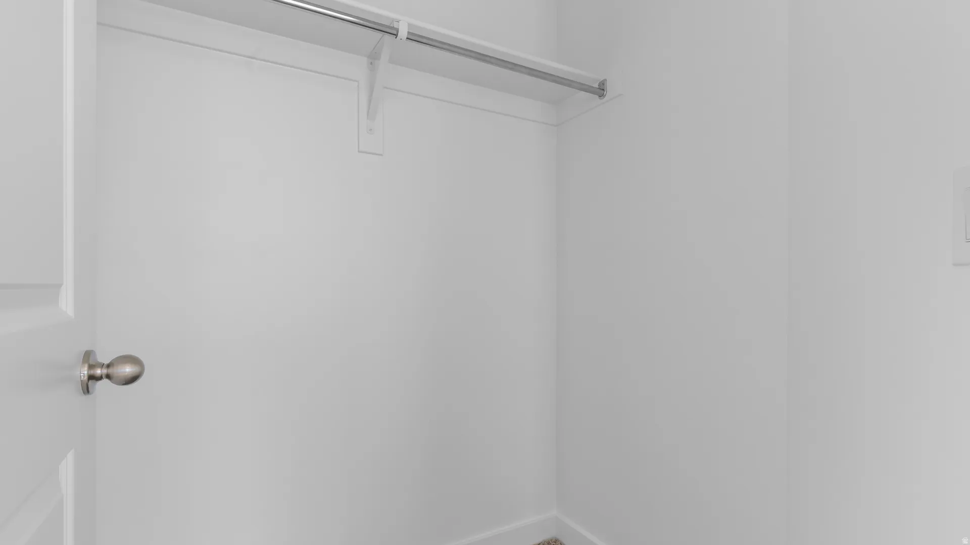 White interior closet featuring a metal hanging rod, integrated shelf, and white painted walls
