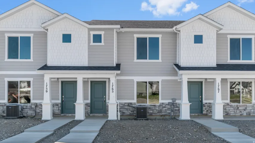 Contemporary townhome-style exterior featuring light gray siding, white trim accents, and stone veneer detailing