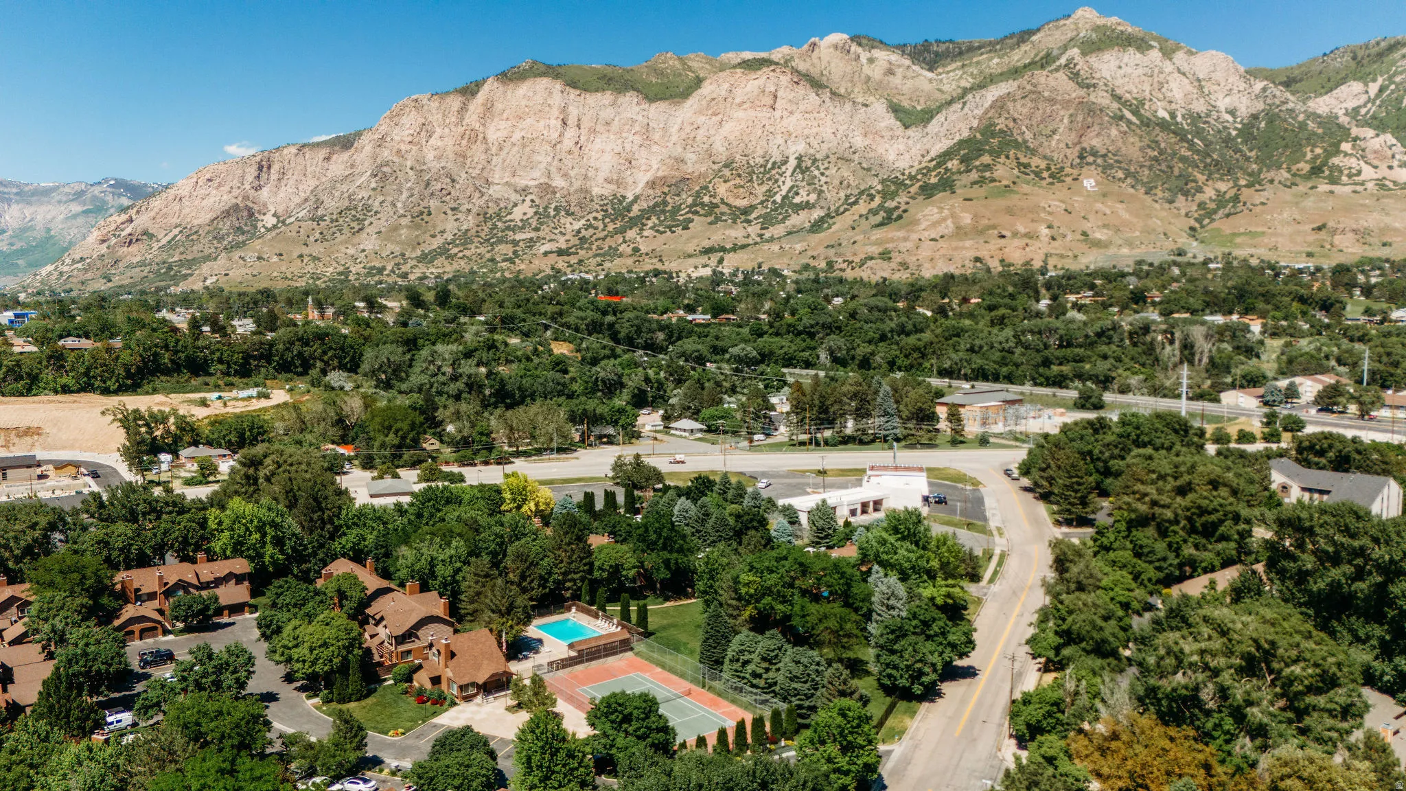 Aerial perspective showcasing a residential community with abundant mature trees, a visible swimming pool, and a tennis court