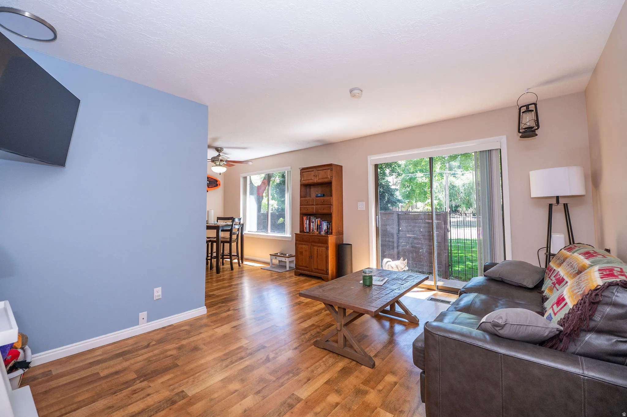 Wood-finish flooring throughout the main living area, featuring a sliding glass door to the exterior, and a dining area with a ceiling fan