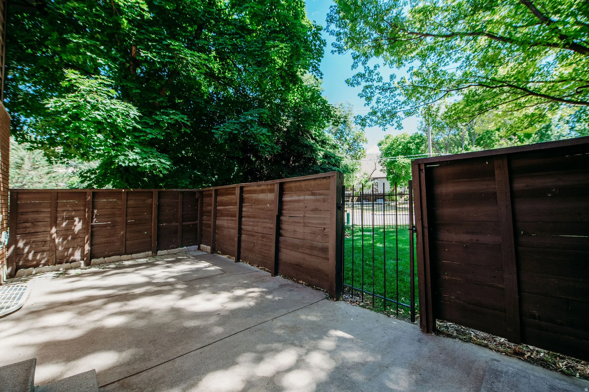 Private concrete patio area with wood-panel fencing, featuring a black metal gate opening to a grassy expanse