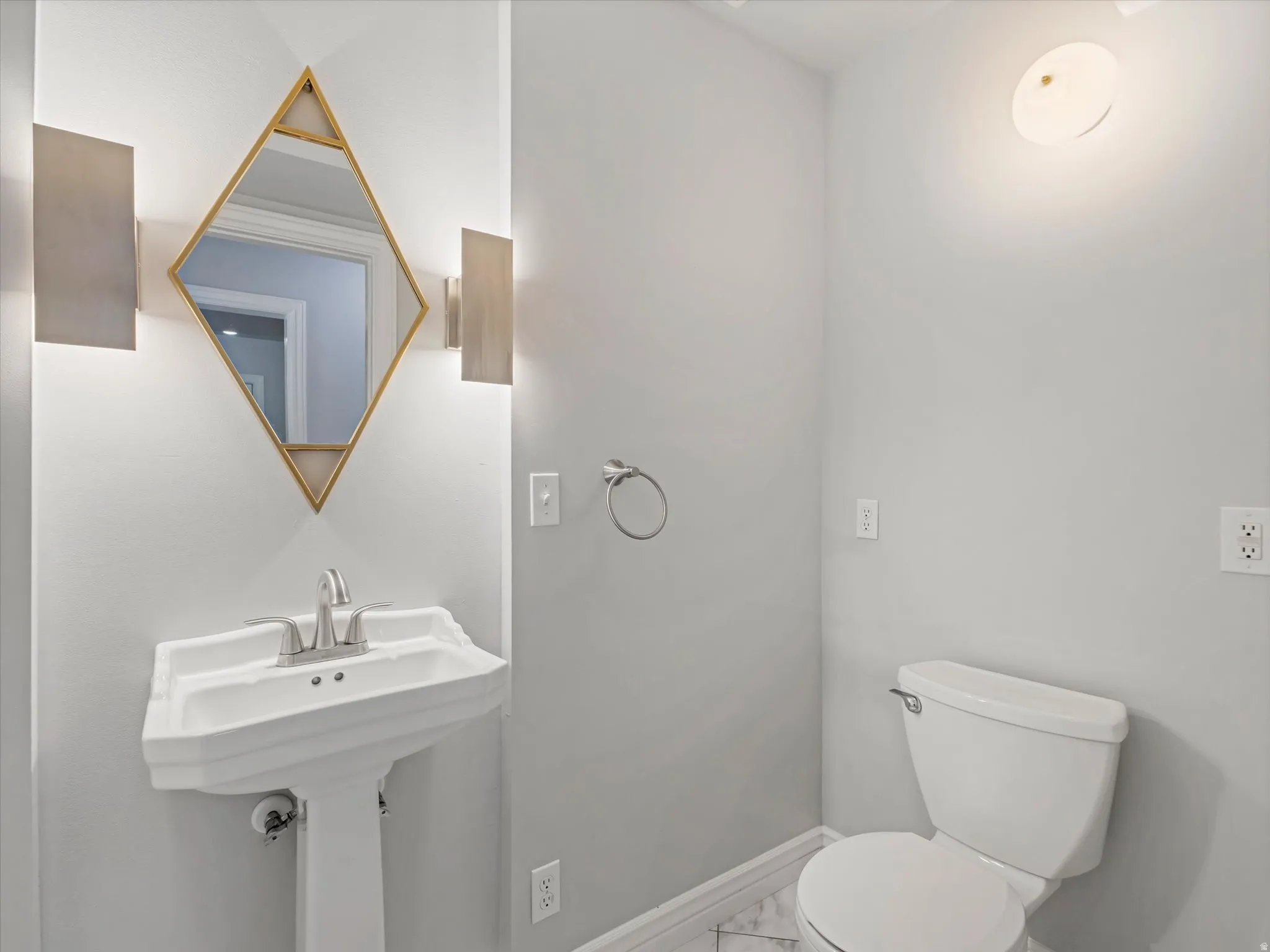 Powder room featuring a white pedestal sink with a chrome faucet, a unique geometric mirror with gold-tone accents, and two wall-mounted sconces