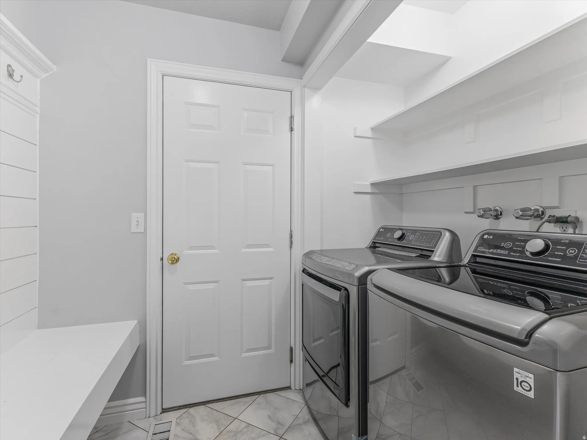 Laundry area with tile flooring, built-in shelving, white paneled door, and a built-in bench