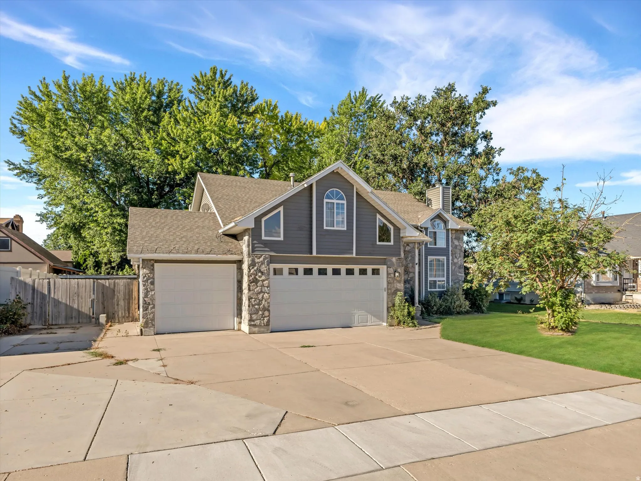 Exterior featuring gray siding, stone accents, multiple garage bays, and a gabled roofline