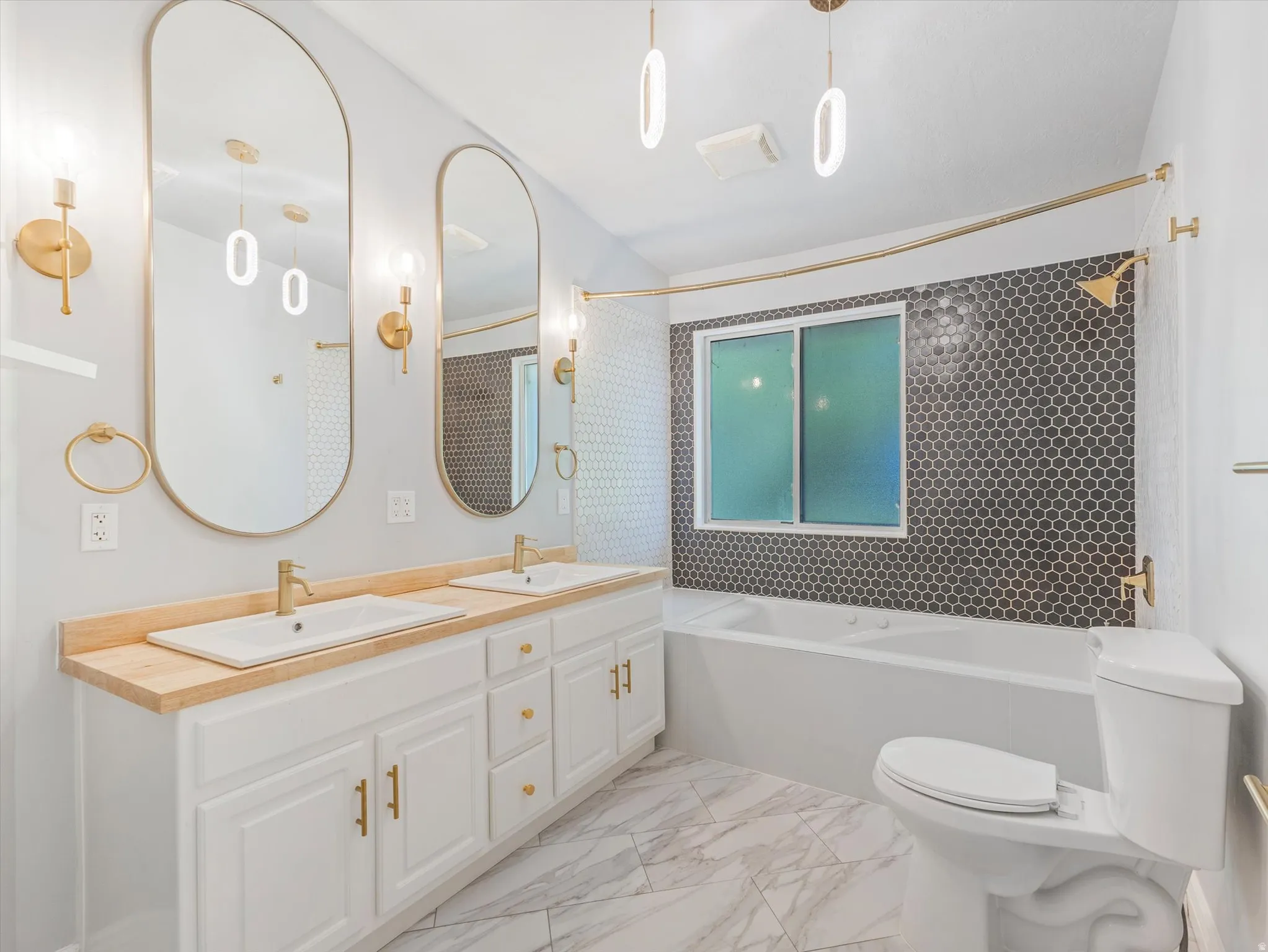 Bathroom featuring a double vanity with wood-finish countertop, white cabinetry, and gold-tone hardware