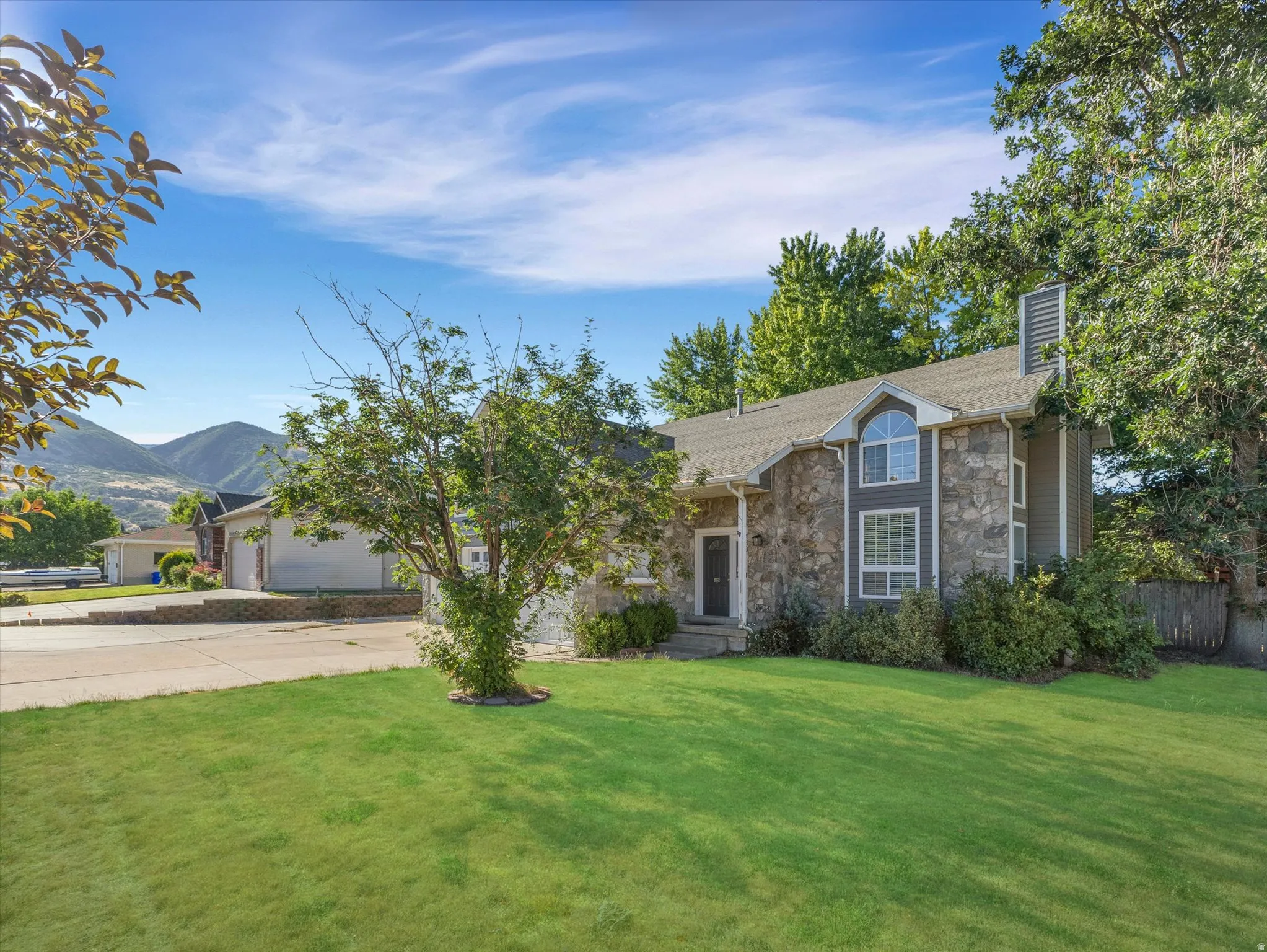 Stone and siding exterior with a prominent arched window and a grey shingle roof