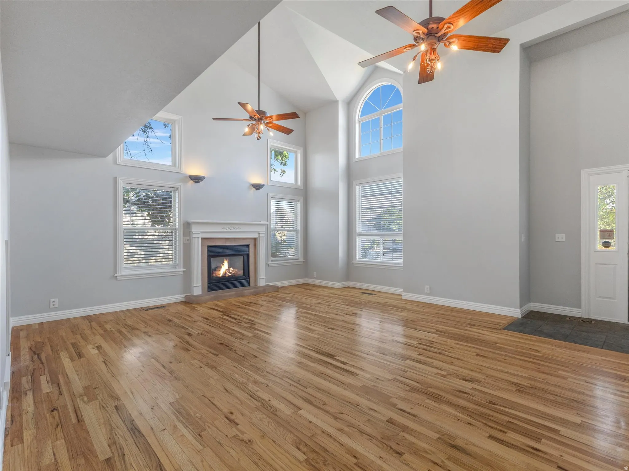 Spacious living area featuring vaulted ceilings, wood-finish flooring, and a fireplace with a decorative mantel