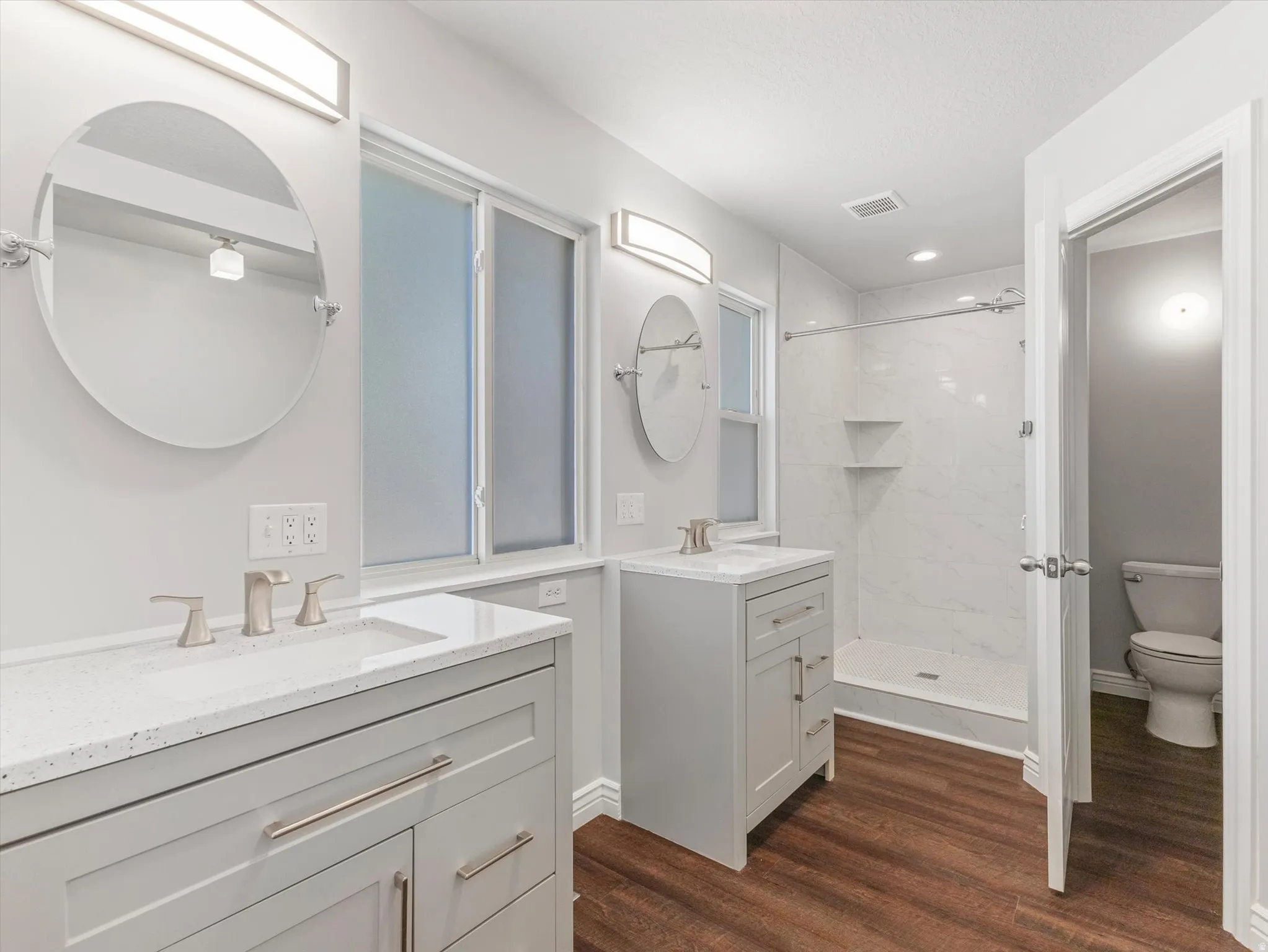 Bathroom featuring dual vanity sinks with light gray cabinetry, white countertops, and brushed nickel fixtures