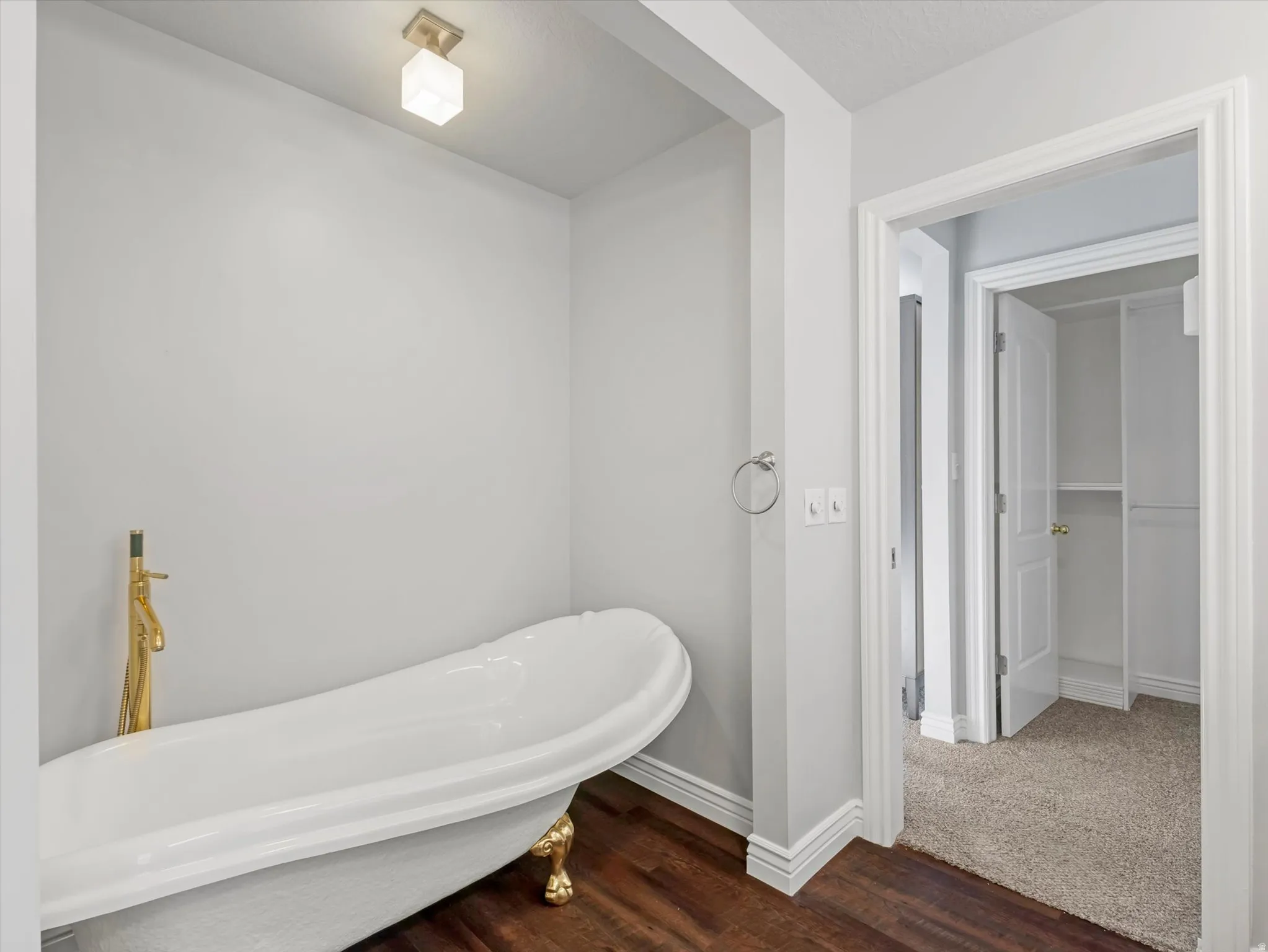 Freestanding clawfoot tub with a gold-finish faucet, dark wood-finish flooring, and white baseboards