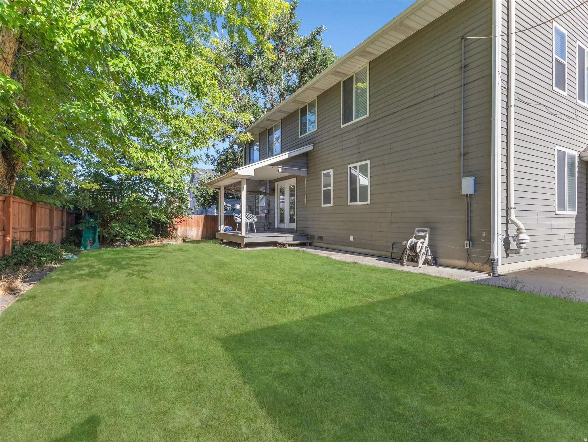 Spacious backyard featuring a manicured lawn, wood fencing, and mature trees providing natural shade