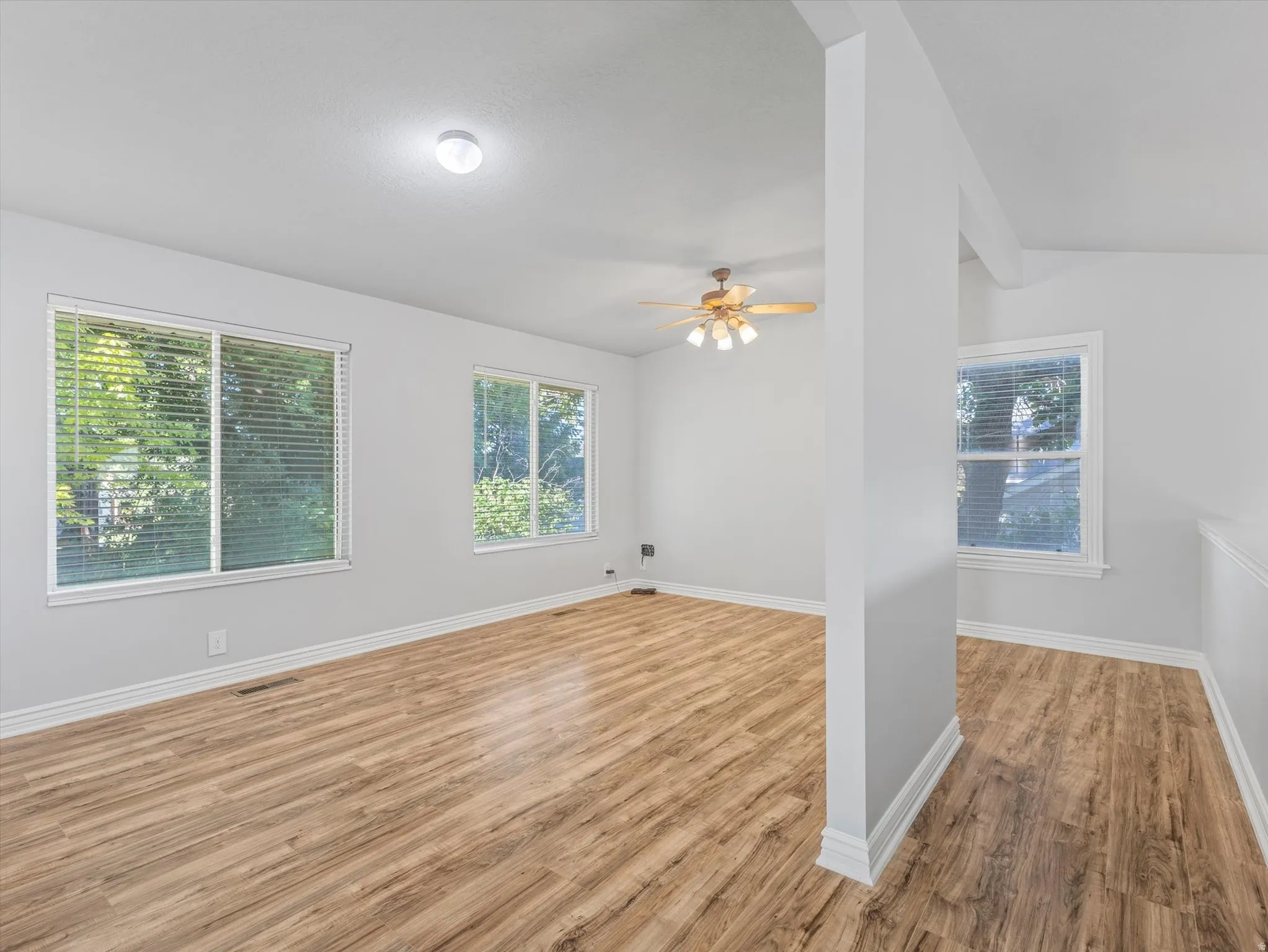 Bright interior featuring wood-finish flooring, multiple windows with natural light, a ceiling fan, and white baseboards