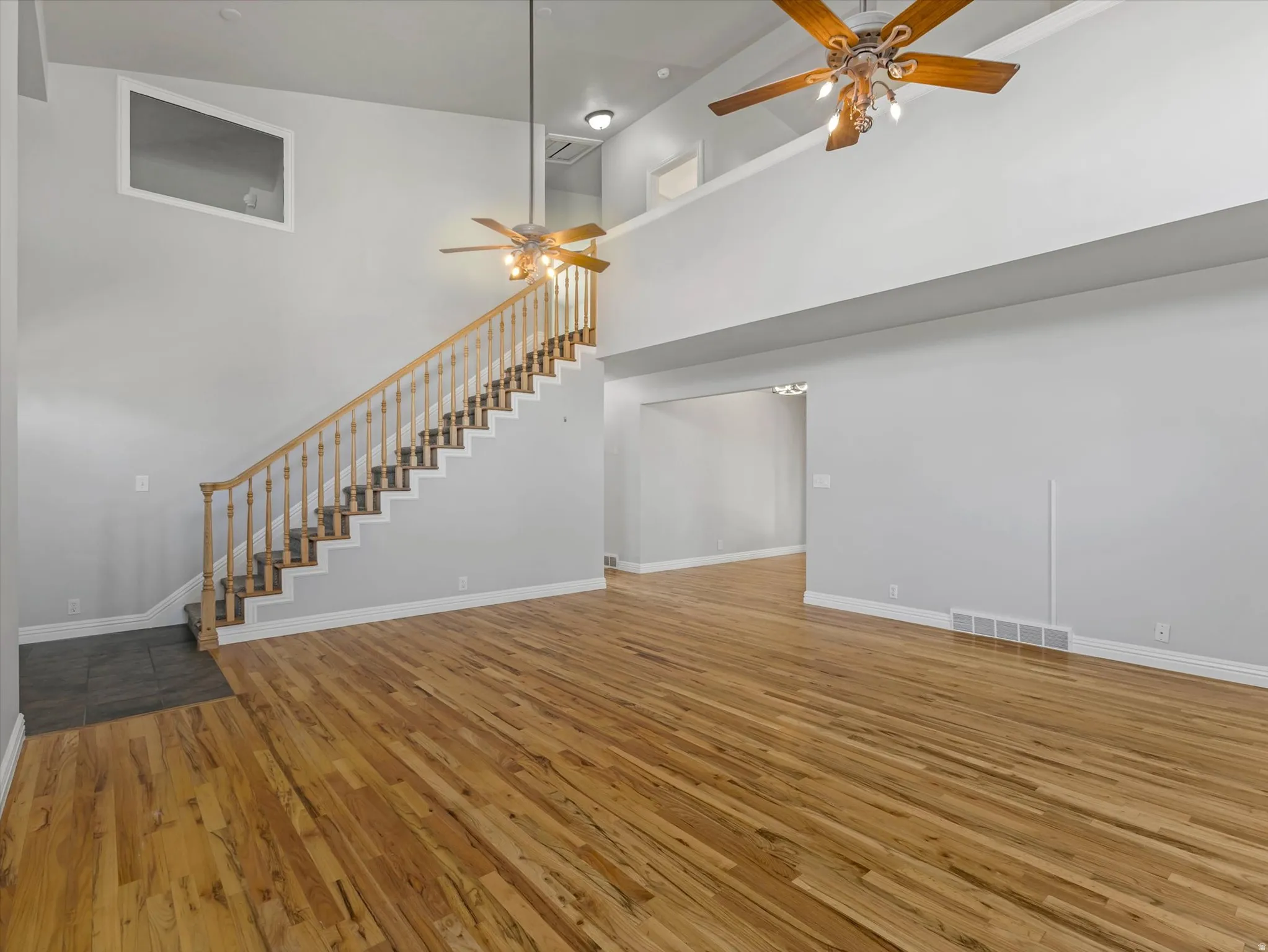 Spacious living area featuring high vaulted ceilings, light wood-finish flooring, and a grand staircase with natural wood balusters