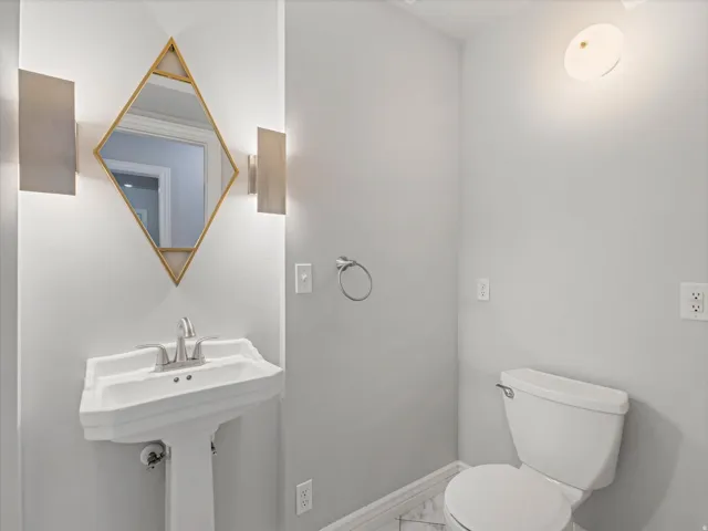 Powder room featuring a white pedestal sink with a chrome faucet, a unique geometric mirror with gold-tone accents, and two wall-mounted sconces