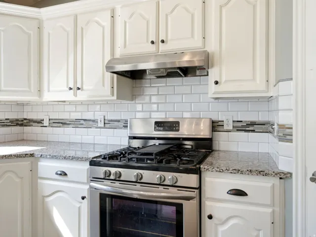 Kitchen featuring white cabinetry, granite-style countertops, stainless steel range with overhead vent, and subway tile backsplash with decorative mosaic accents