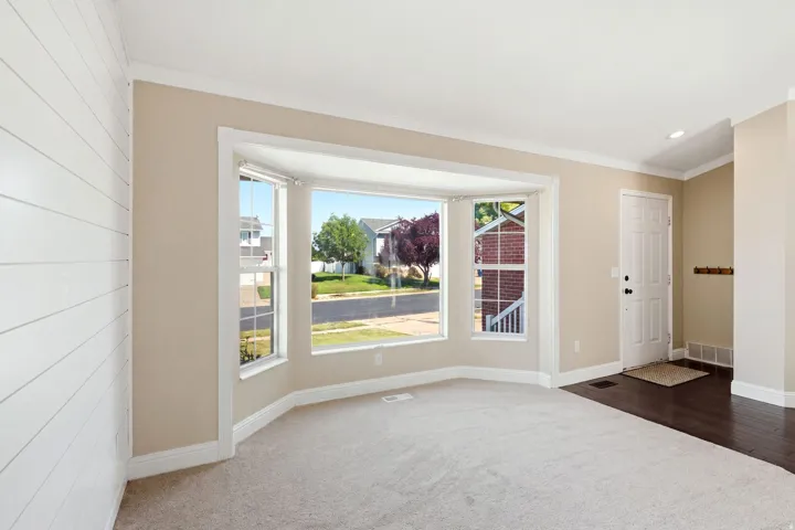 Bay window with broad trim, light carpeting, wood-finish flooring, white shiplap accent wall, and a white entry door
