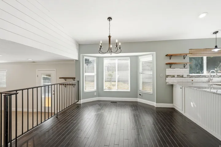 Open-concept space featuring dark wood-finish flooring, a bay window with blinds, and an iron chandelier