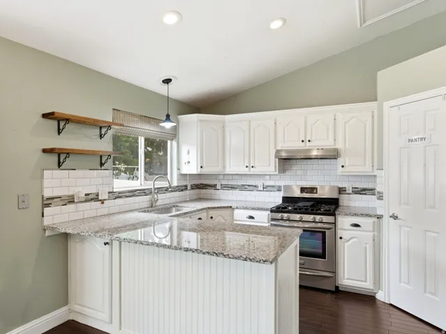 Kitchen featuring white cabinetry, light-toned countertops, a stainless steel range with overhead hood, and a subway tile backsplash
