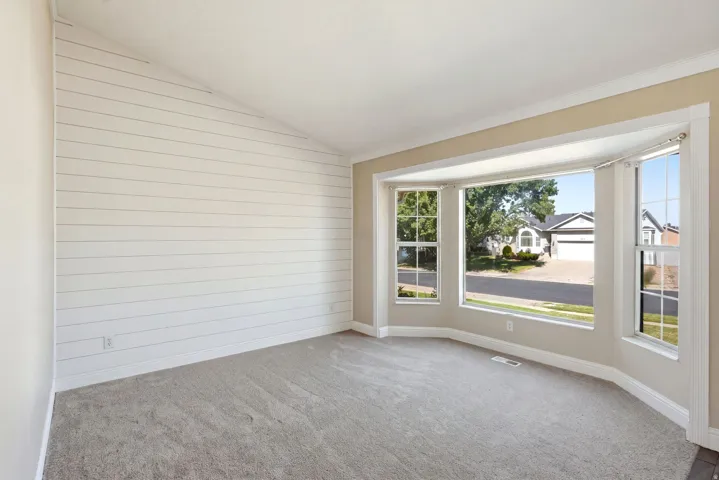 Spacious room featuring a prominent bay window, shiplap accent wall, vaulted ceiling, neutral paint tones, and grey carpeting