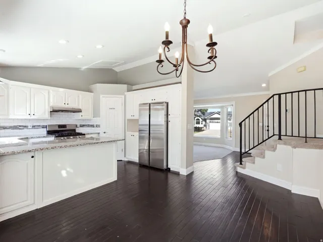 Open-concept living space featuring dark wood-finish flooring, a white kitchen with granite countertops, stainless steel appliances, and a subway tile backsplash