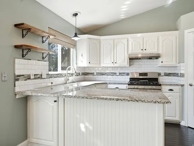 Kitchen featuring white cabinetry, granite countertops, subway tile backsplash, stainless steel gas range, and a breakfast bar with beadboard paneling