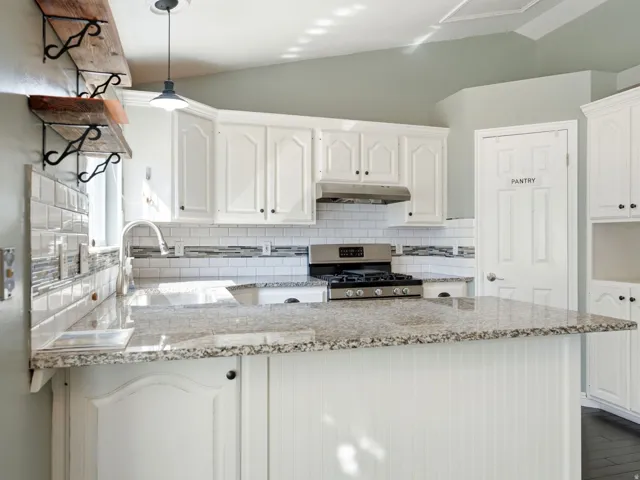 Kitchen featuring white cabinetry, granite countertops, stainless steel appliances, a tile backsplash, and beadboard paneling on the island