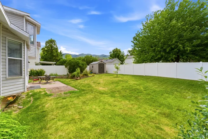 Expansive grass yard with a white privacy fence, concrete patio, and garden shed