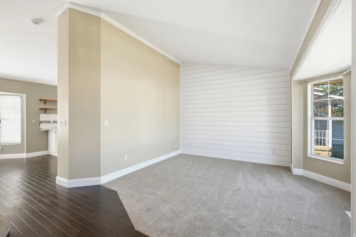 Carpeted living area featuring a shiplap accent wall, a bay window, and crown molding