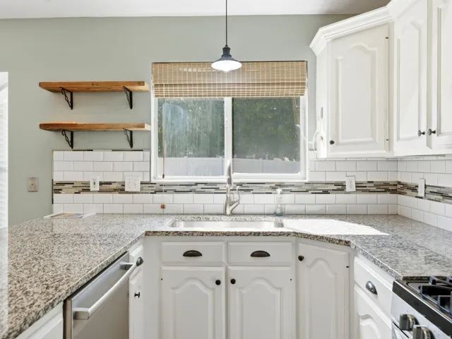 Kitchen featuring white cabinetry, granite countertops, stainless steel appliances, open shelving, and a subway tile backsplash with decorative accent banding