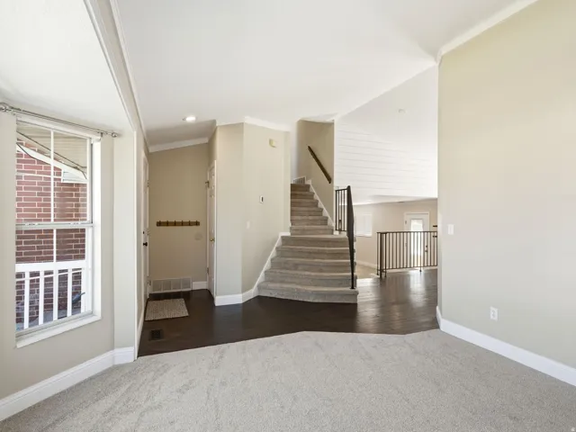 Inviting entryway featuring dark wood-finish flooring, a carpeted staircase with a black metal railing, and light-toned wall finishes