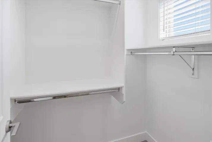 Walk-in closet featuring white shelving, chrome hanging rods, and a window with blinds