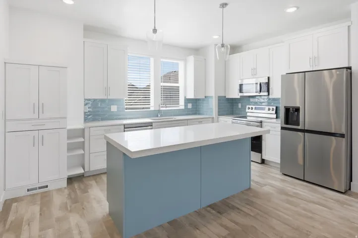 Modern kitchen featuring a blue island with a light-toned countertop, light wood-finish flooring, white cabinetry, stainless steel appliances, and a tiled blue backsplash