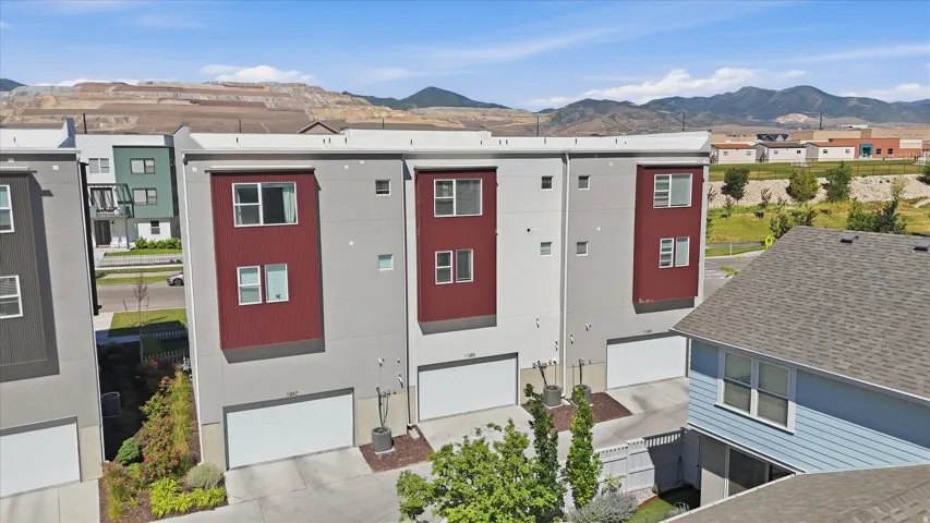 Modern townhome exterior featuring a gray and red facade, multiple windows, an integrated garage, and a paved driveway