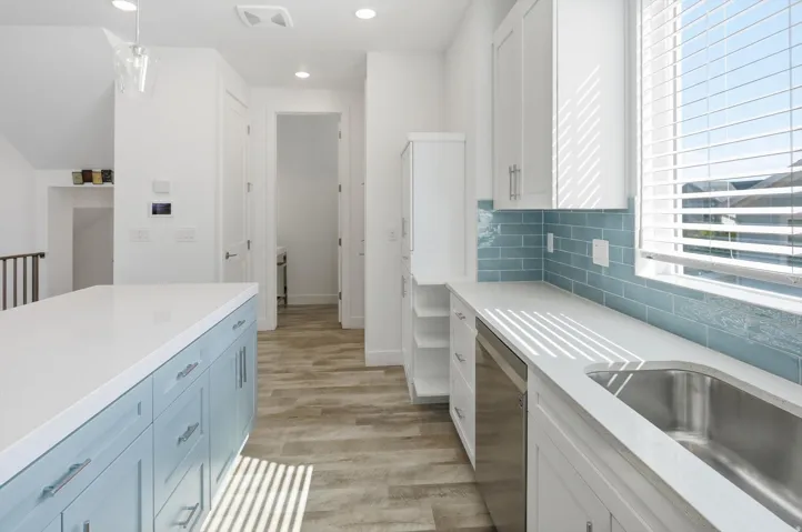Contemporary kitchen featuring a large island with blue cabinetry, light-toned countertops, white upper and lower cabinetry, a stainless steel undermount sink, and a blue subway tile backsplash