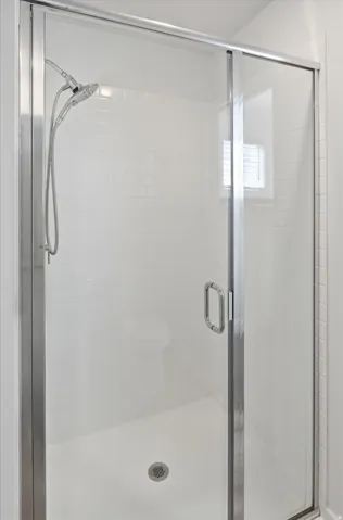 Enclosed shower featuring clear glass doors, subway tile surround, a built-in shower head, and an integrated window for natural light