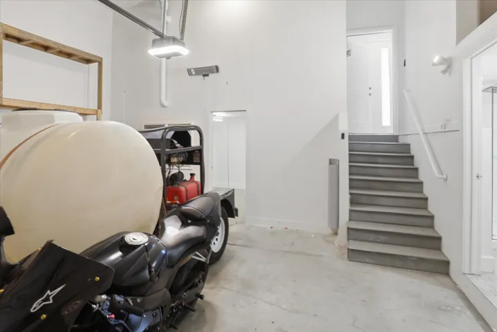 Concrete flooring in garage featuring a staircase with a white railing and a white door with vertical glass insert