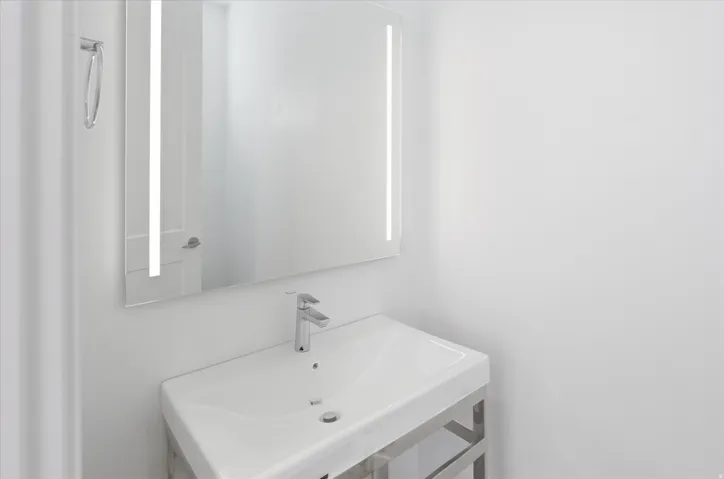 Contemporary bathroom featuring a rectangular vessel sink with a chrome faucet, stainless steel vanity frame, and an illuminated mirror with vertical lighting