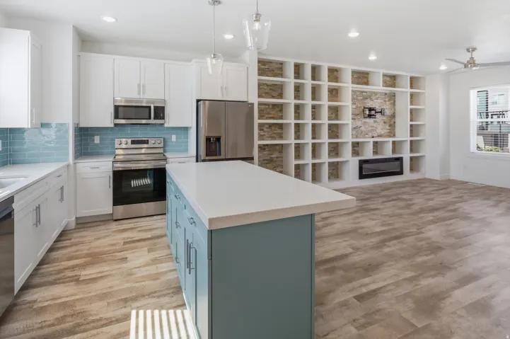 Open-concept living space with wood-finish flooring, a contemporary kitchen, and a built-in entertainment wall