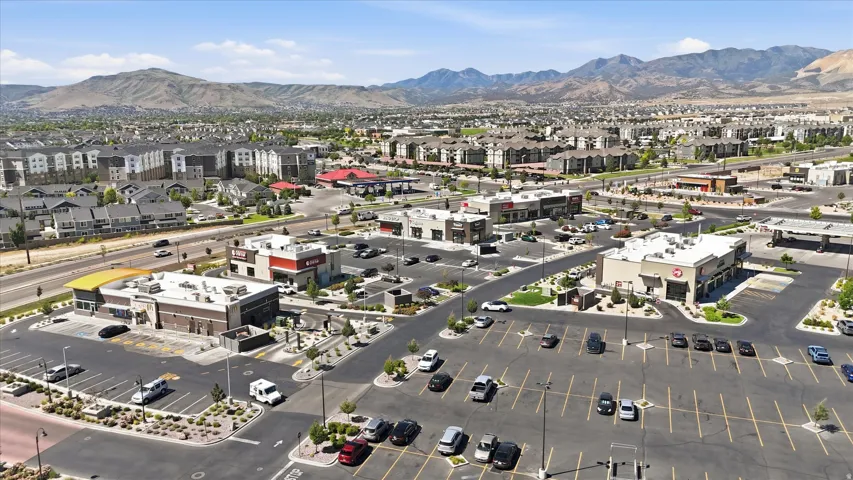 Commercial retail center with multiple buildings, extensive surface parking, and mountainous terrain in the background
