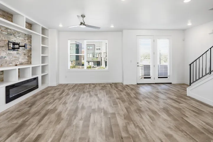 Spacious living area featuring wood-finish flooring, a built-in entertainment center with stone-look accent wall and electric fireplace, and a ceiling fan