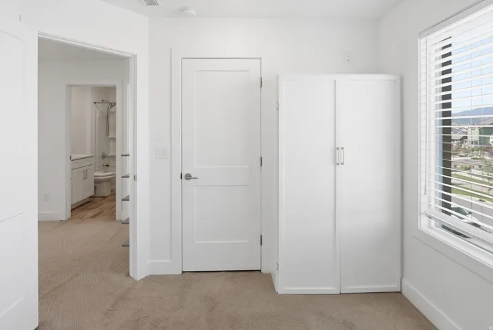 Interior room featuring light carpeting, white walls, and a window with horizontal blinds