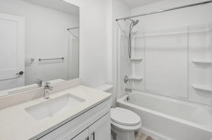 Bathroom featuring a white vanity with an undermount sink, a light-toned countertop, a large wall-mounted mirror, a polished chrome faucet, and a white bathtub with an integrated shower