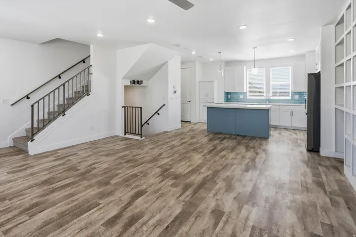 Spacious living area featuring wood-finish flooring, a modern kitchen with a blue island, white cabinetry, and a blue tile backsplash